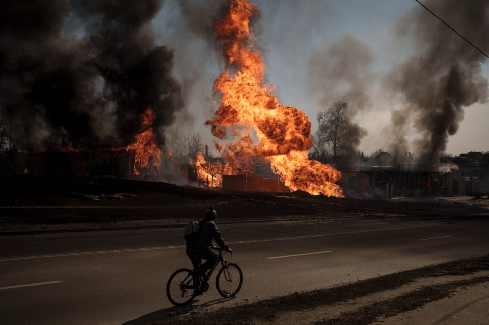 Ένας άνδρας οδηγεί το ποδήλατό του μπροστά από φλόγες και καπνό που αναδύεται από φωτιά μετά από ρωσική επίθεση στο Χάρκοβο της Ουκρανίας, Παρασκευή 25 Μαρτίου του 2022. (AP Photo/Felipe Dana)